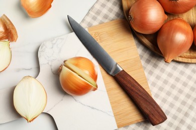 Photo of Whole and cut onions with knife on white marble table, flat lay