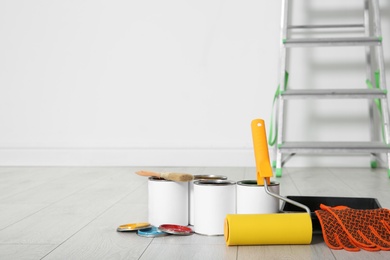 Photo of Cans of paint and decorator tools on wooden floor indoors. Space for text