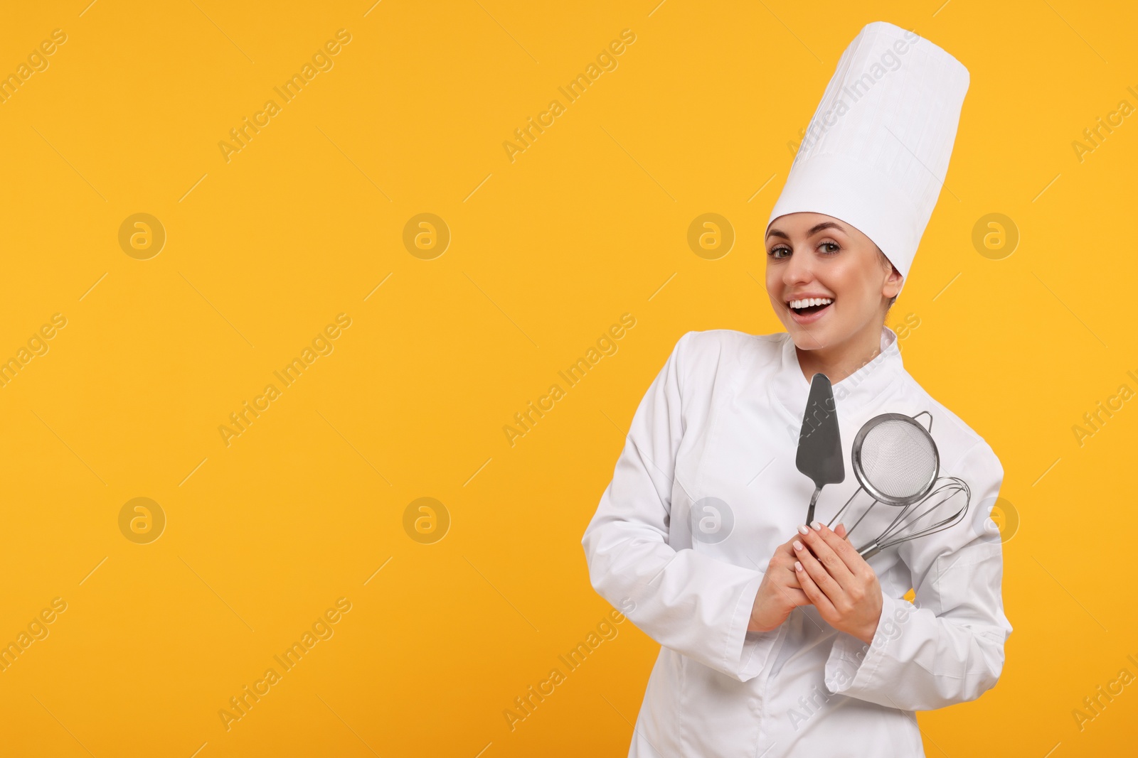 Photo of Happy confectioner in uniform holding professional tools on yellow background. Space for text