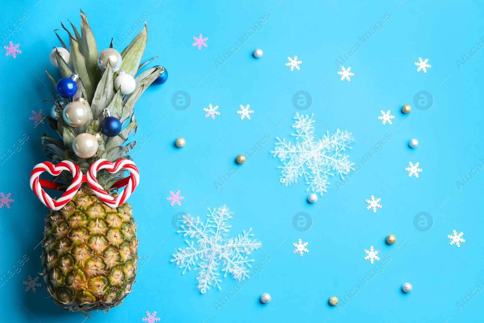 Photo of Pineapple with funny glasses and Christmas decor on light blue background, flat lay. Creative concept