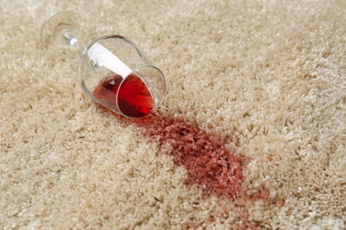 Photo of Overturned glass and spilled red wine on soft carpet, closeup