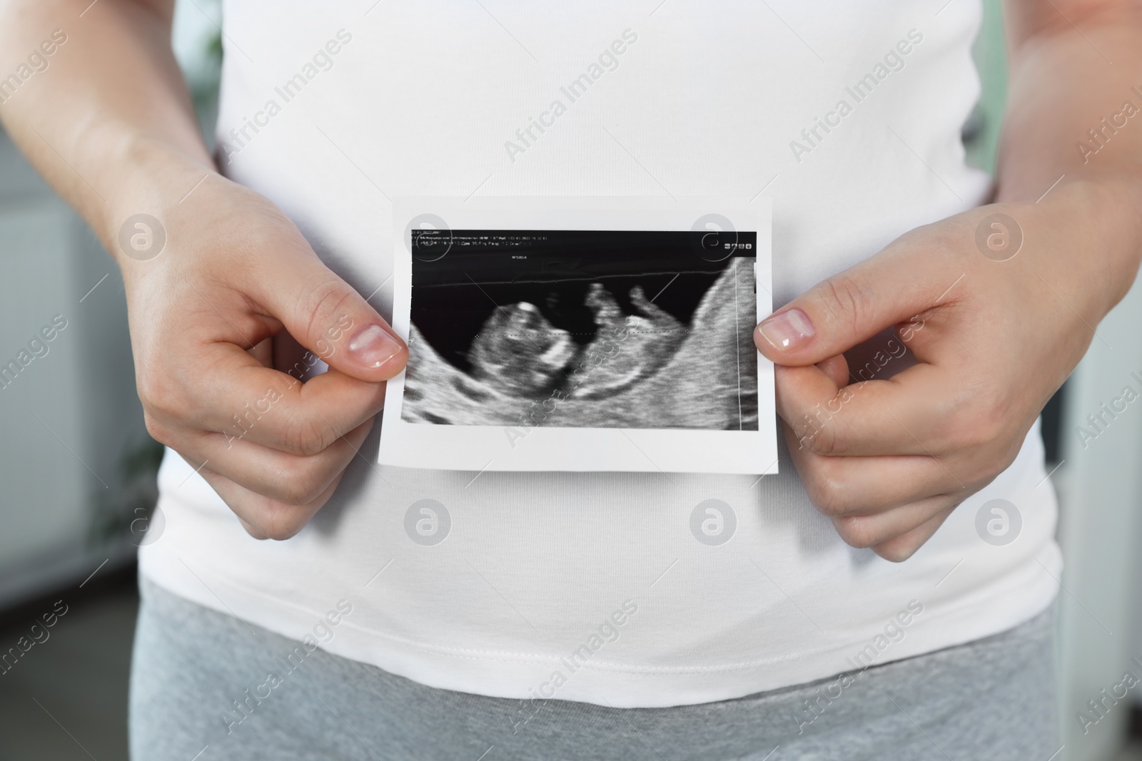 Photo of Pregnant woman with ultrasound picture of baby indoors, closeup