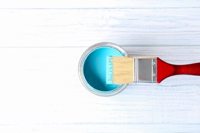 Tin can with paint and brush on wooden background, top view