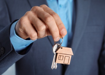 Photo of Young man holding house key with trinket, closeup