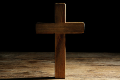 Christian cross on wooden table against black background. Religion concept