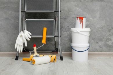 Photo of Metallic folding ladder and painting tools near grey wall indoors