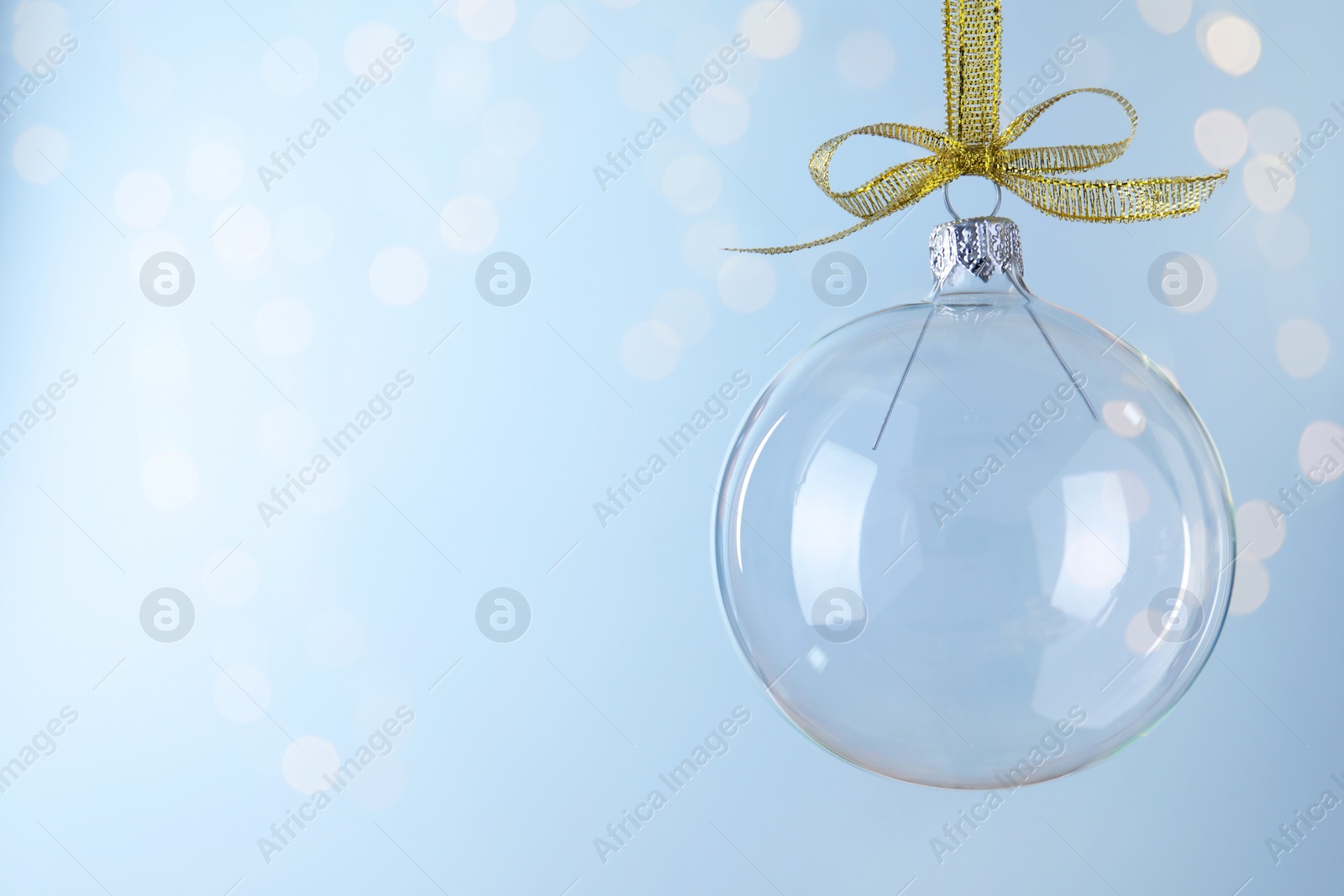 Photo of Transparent glass Christmas ball against light background with festive lights. Space for text