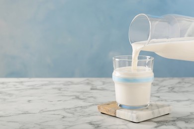 Pouring fresh milk into glass on white marble table, space for text