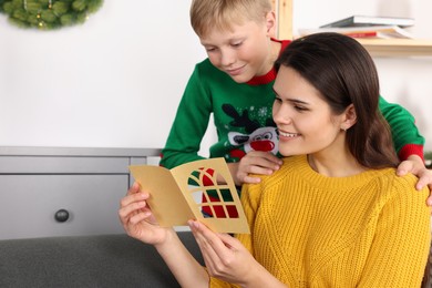 Happy woman receiving greeting card from her son at home