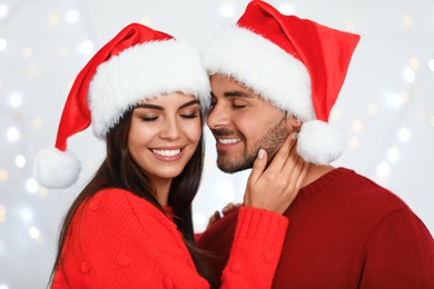 Photo of Lovely young couple in Santa hats against blurred festive lights. Christmas celebration