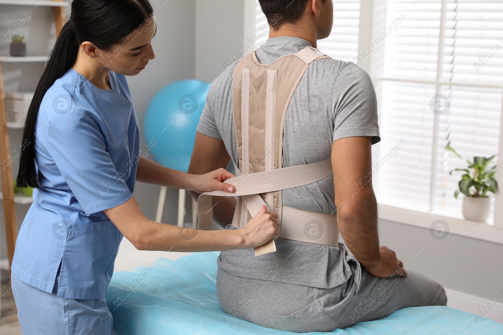 Photo of Orthopedist helping patient to put on posture corrector in clinic. Scoliosis treatment