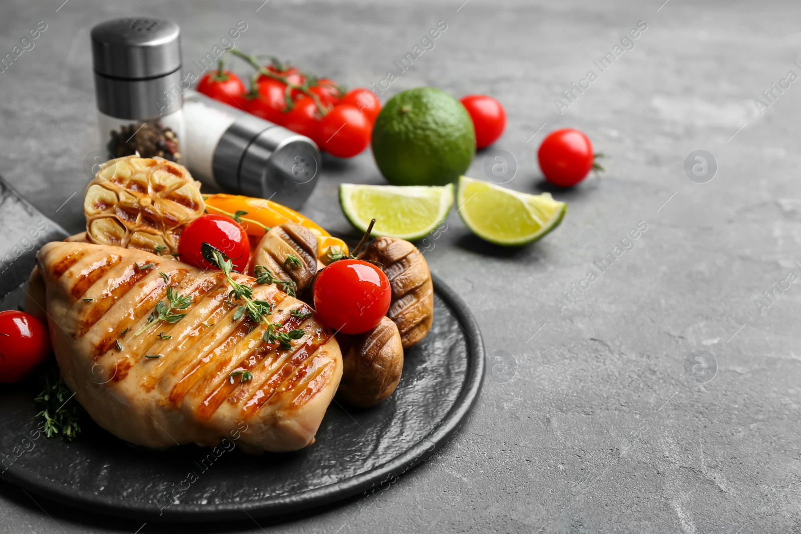 Photo of Tasty grilled chicken fillet with tomatoes and thyme on grey table, closeup