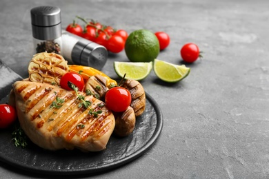 Photo of Tasty grilled chicken fillet with tomatoes and thyme on grey table, closeup