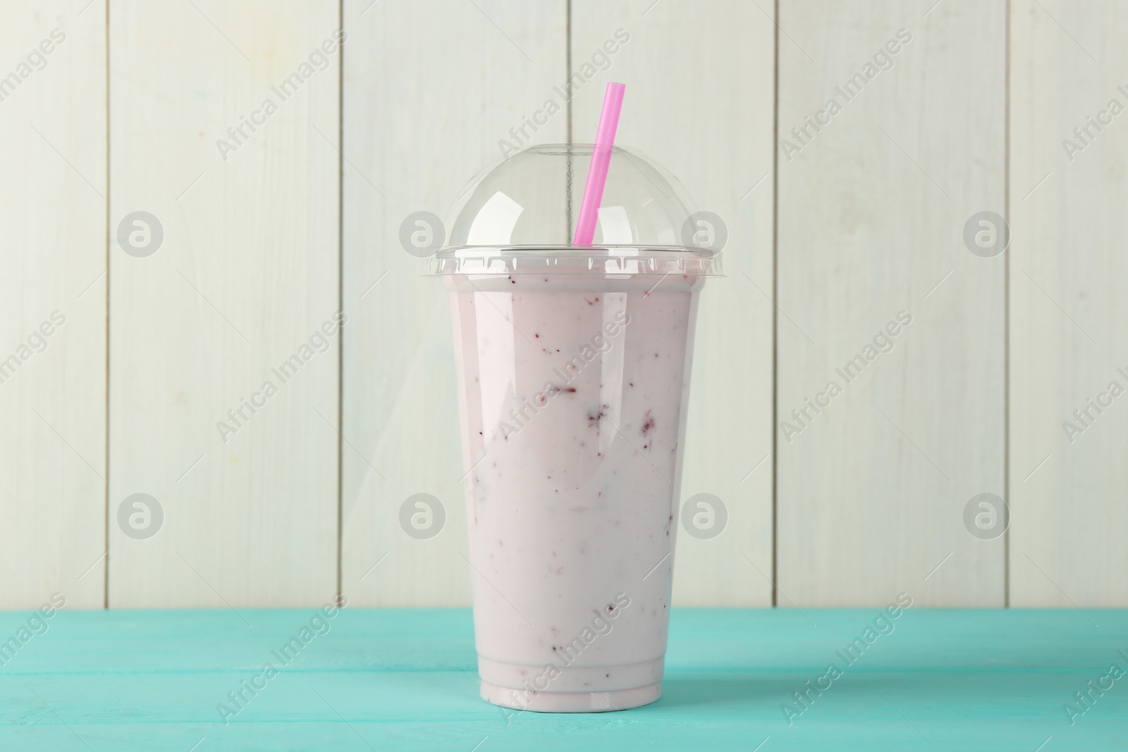 Photo of Tasty smoothie in plastic cup on light blue table against white wooden wall