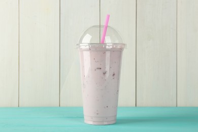 Photo of Tasty smoothie in plastic cup on light blue table against white wooden wall