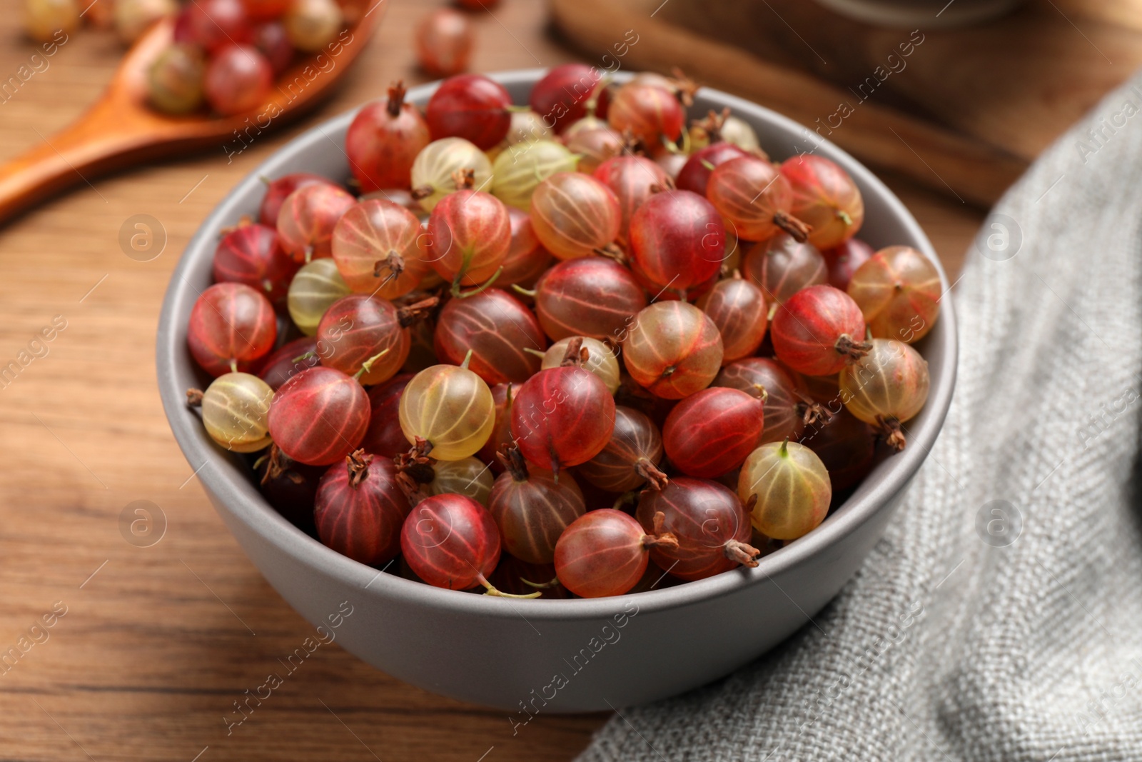 Photo of Bowl full of ripe gooseberries on wooden table, closeup
