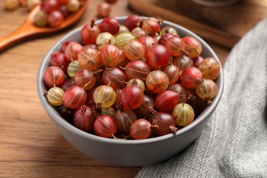 Bowl full of ripe gooseberries on wooden table, closeup