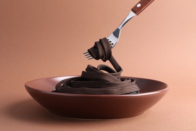 Fork with shoelace above plate on brown background