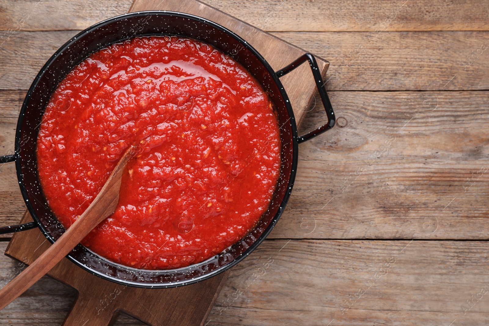 Photo of Delicious tomato sauce in pan on wooden table, top view. Space for text