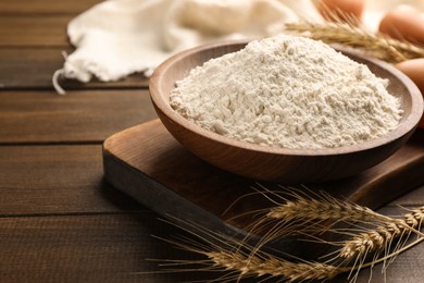 Photo of Bowl with wheat flour and spikelets on wooden table, space for text