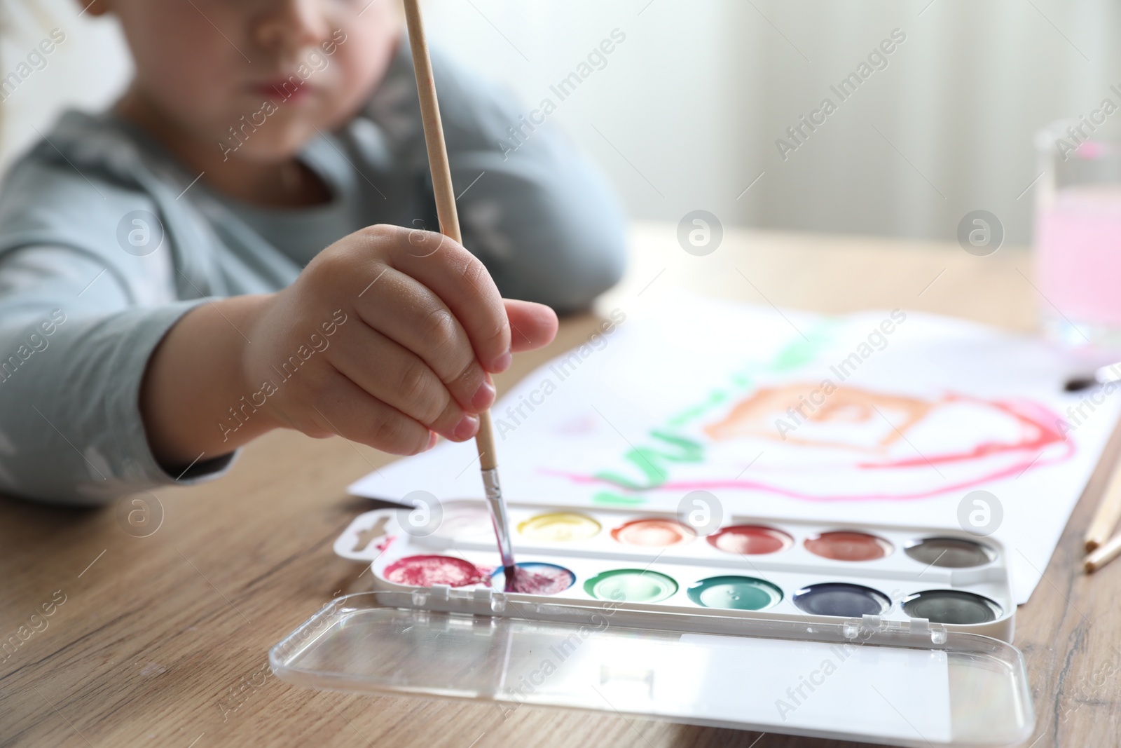 Photo of Little girl with brush drawing at wooden table indoors, selective focus. Child`s art