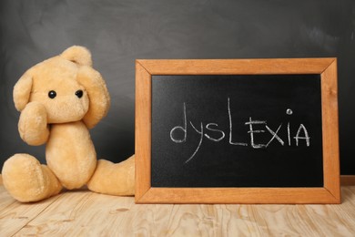 Photo of Teddy bear and small blackboard with word Dyslexia on wooden table