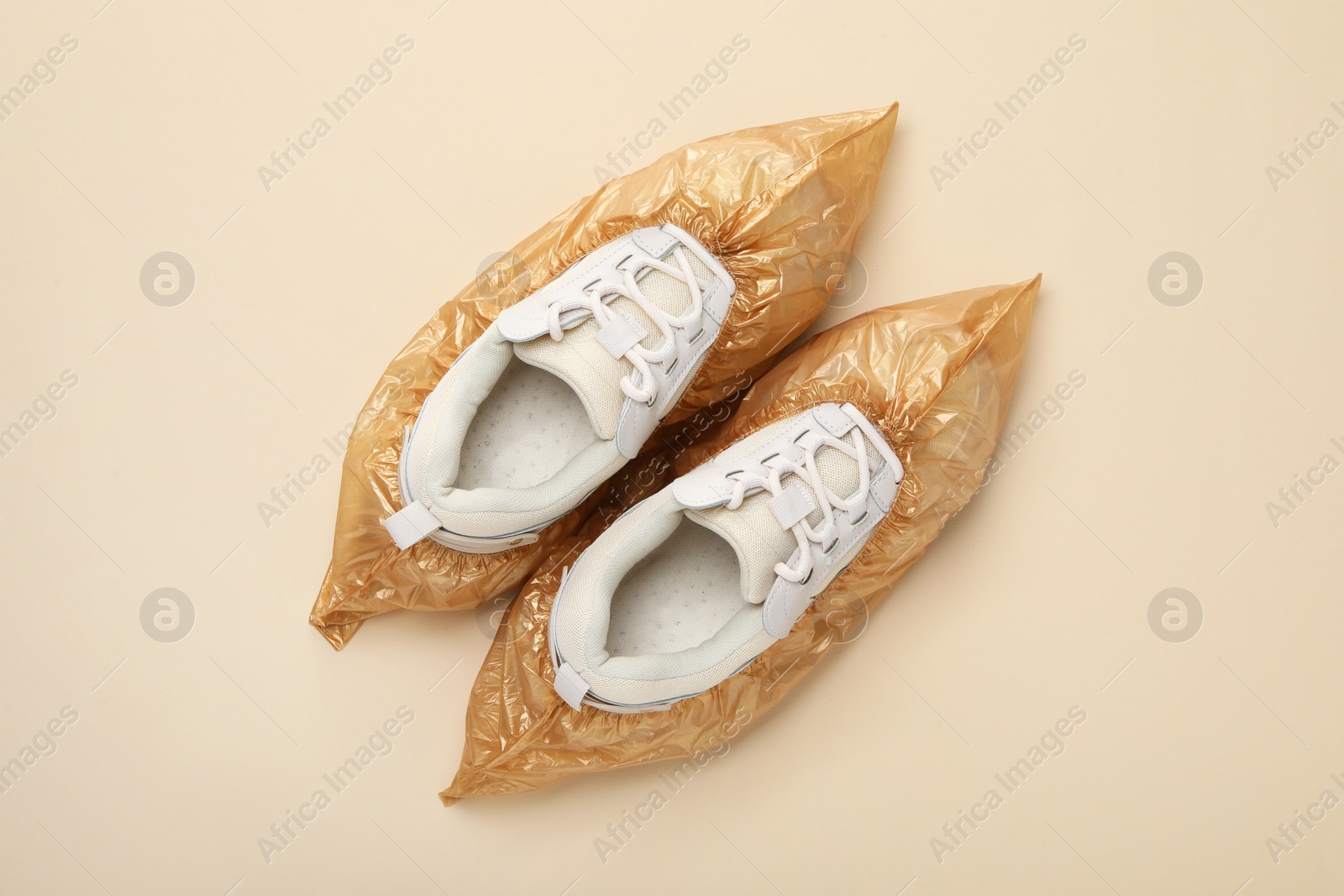 Photo of Sneakers in shoe covers on beige background, top view