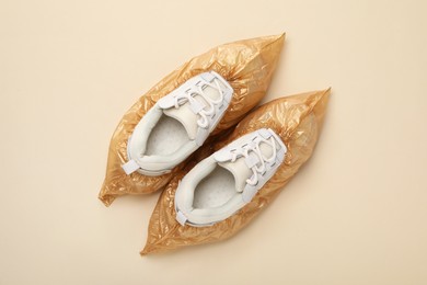 Photo of Sneakers in shoe covers on beige background, top view