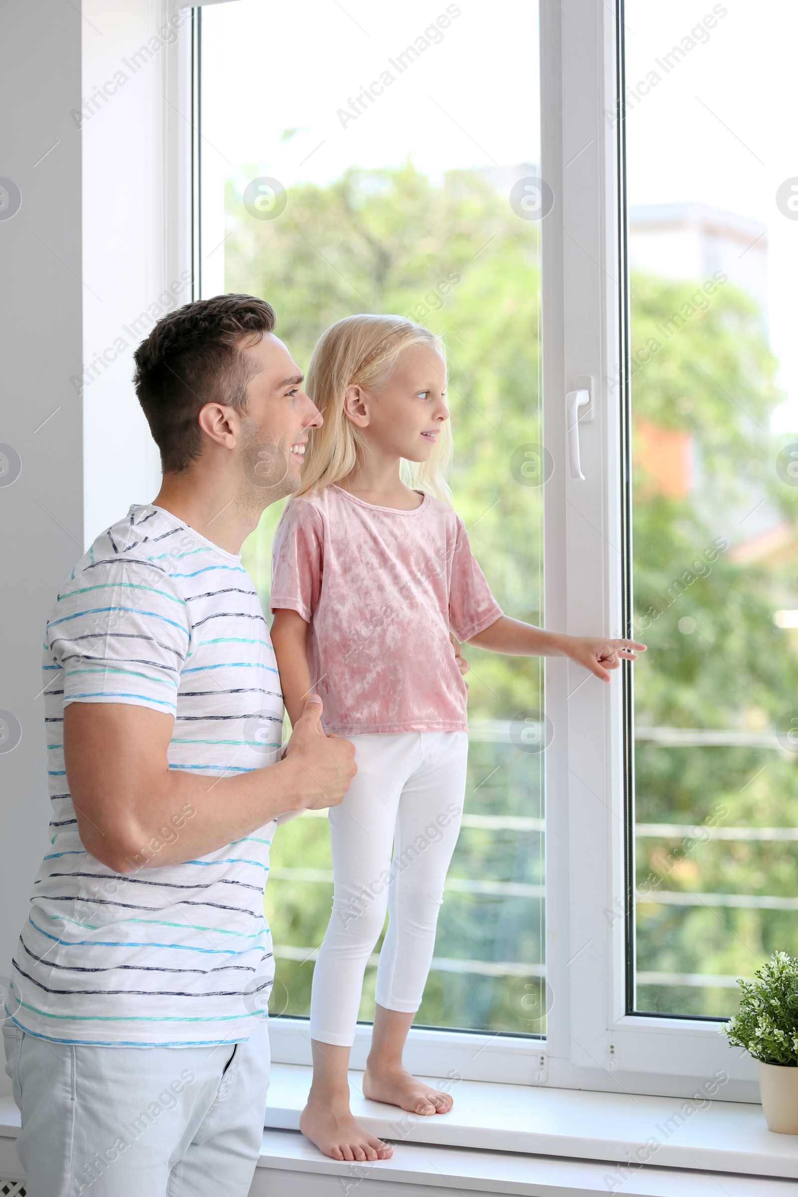 Photo of Young man with cute little girl near window at home