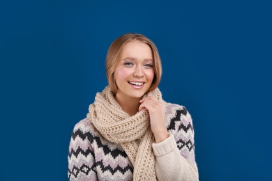 Photo of Young woman in warm sweater and scarf on blue background. Winter season