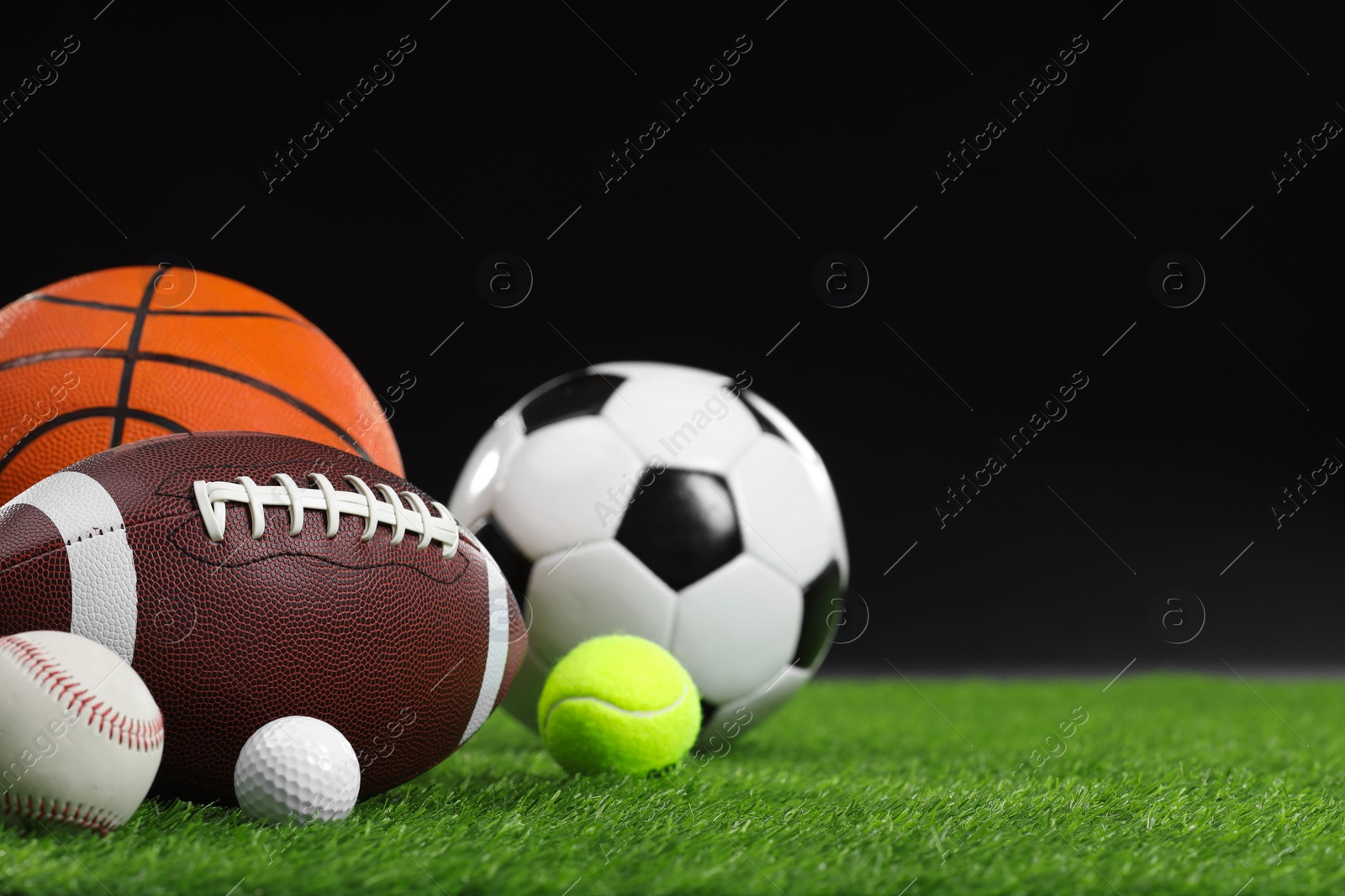 Photo of Many different sports balls on green grass against black background, space for text