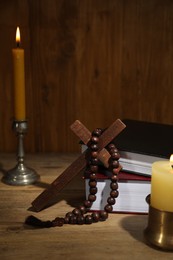Photo of Bible, cross, rosary beads and church candles on wooden table