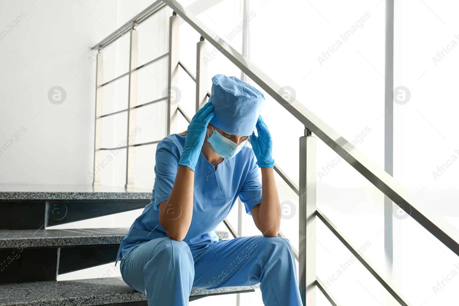 Photo of Exhausted doctor sitting on stairs in hospital. Stress of health care workers during COVID-19 pandemic