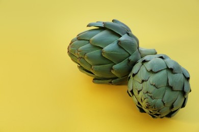 Photo of Whole fresh raw artichokes on yellow background, closeup. Space for text