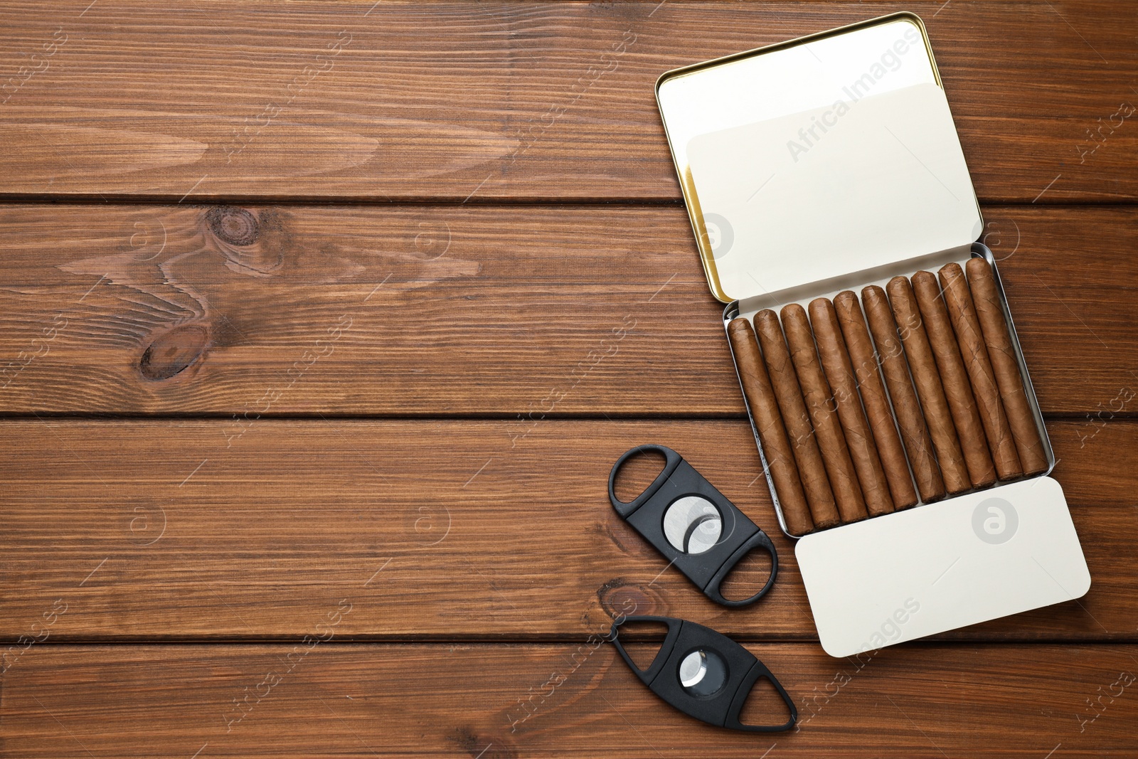 Photo of Humidor with cigars and guillotine cutters on wooden table, flat lay. Space for text