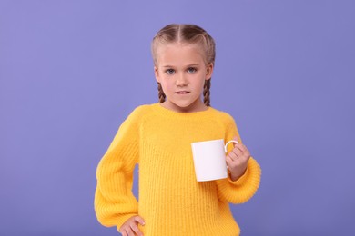 Cute girl with white ceramic mug on violet background
