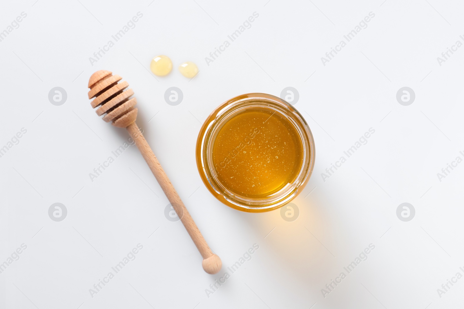 Photo of Tasty honey in glass jar and dipper on white background, top view