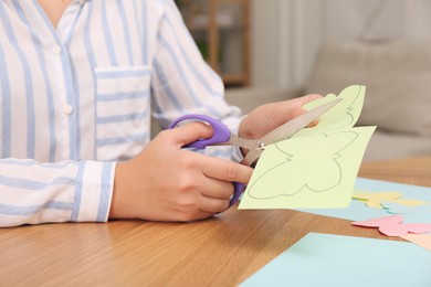 Woman cutting color paper with scissors at wooden table indoors, closeup