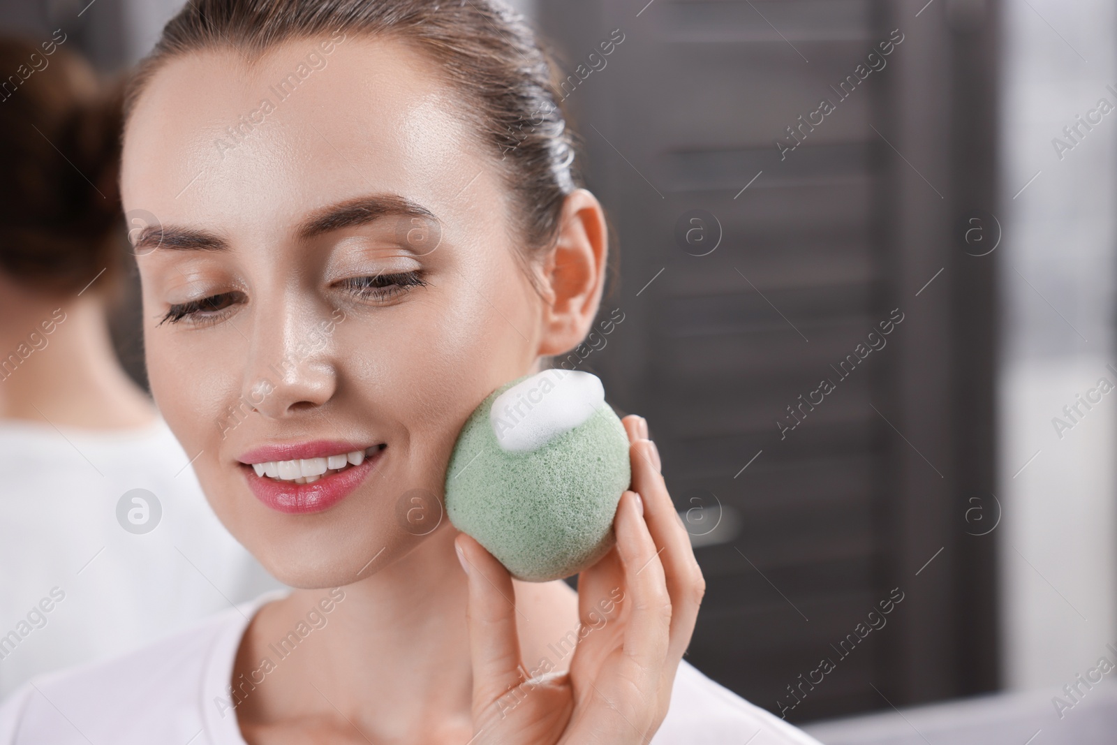 Photo of Happy young woman washing her face with sponge in bathroom. Space for text
