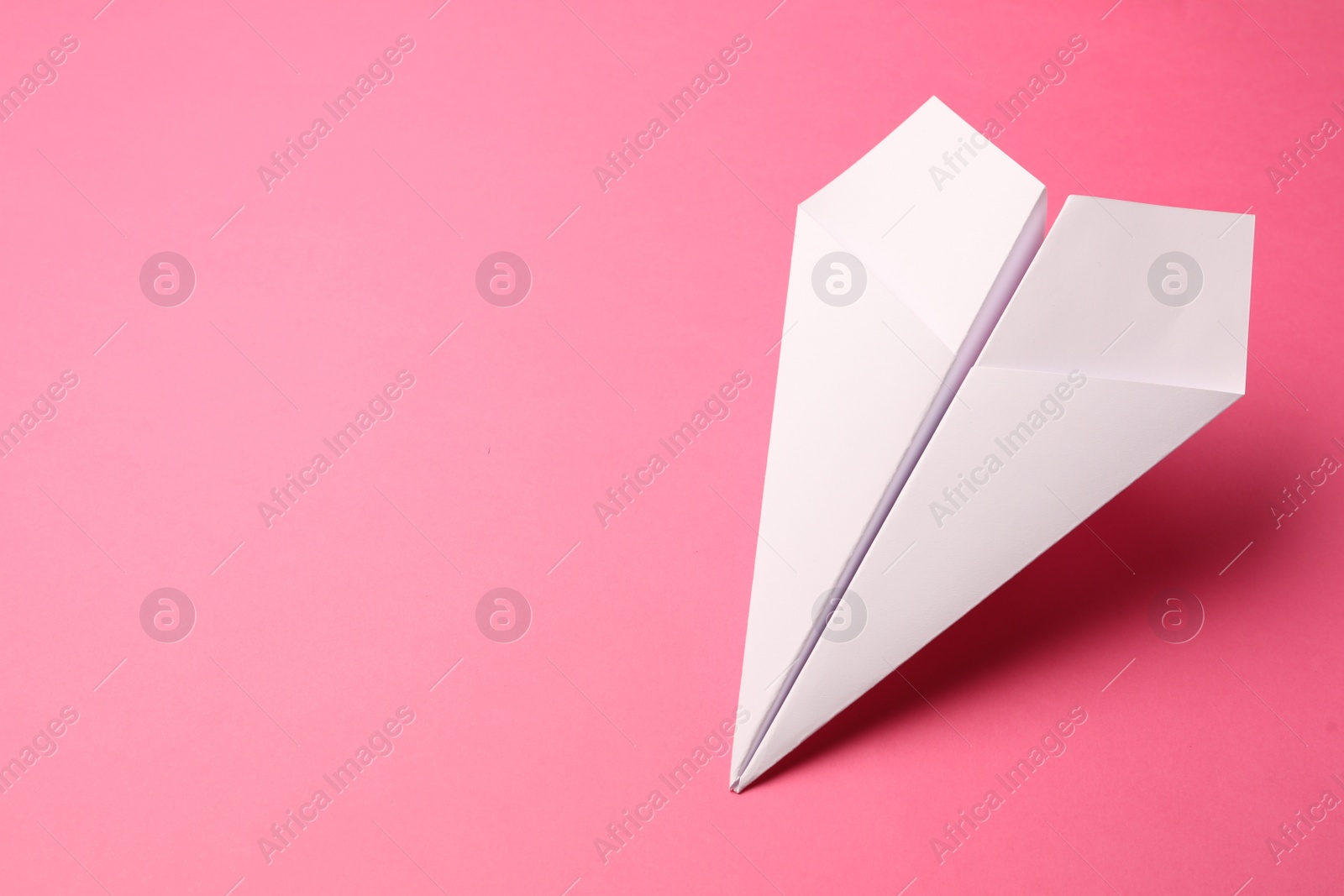 Photo of Handmade white paper plane on pink background, space for text