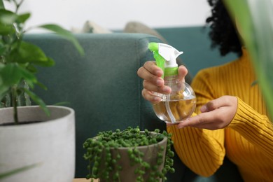 Photo of Woman spraying beautiful potted houseplant with water indoors, closeup