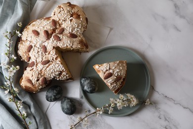 Photo of Delicious Italian Easter dove cake (traditional Colomba di Pasqua), painted eggs and branches with beautiful flowers on white marble table, flat lay