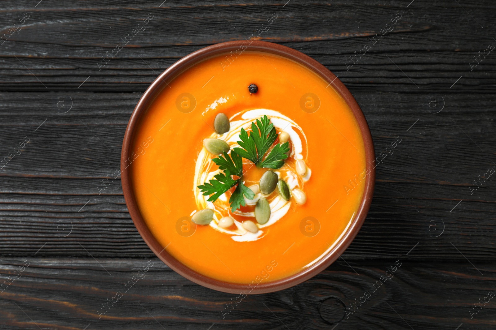 Photo of Delicious pumpkin soup in bowl on wooden table, top view