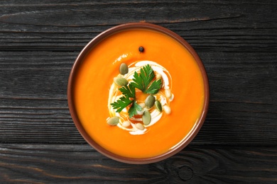 Photo of Delicious pumpkin soup in bowl on wooden table, top view