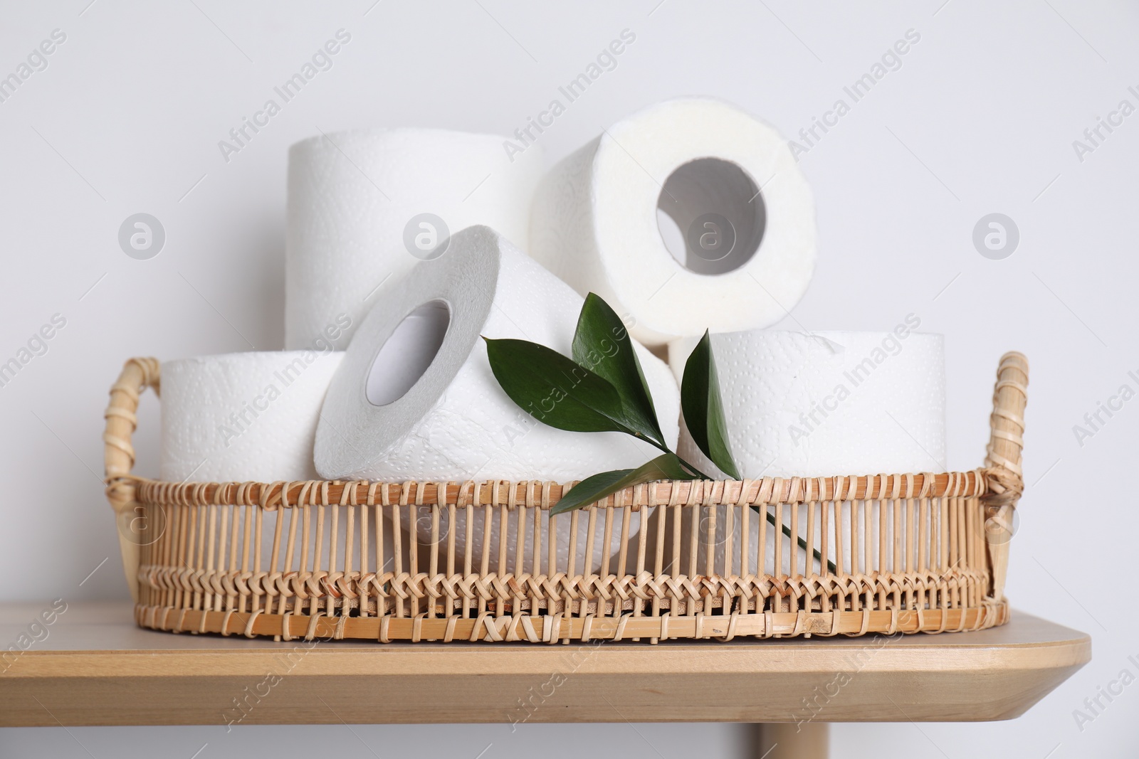 Photo of Toilet paper rolls and green leaves on wooden table near white wall