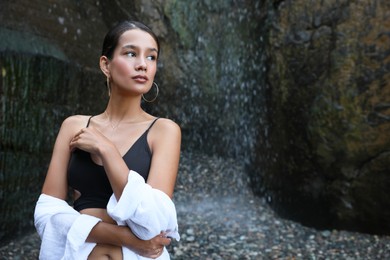 Photo of Beautiful young woman in stylish bikini near waterfall outdoors, space for text