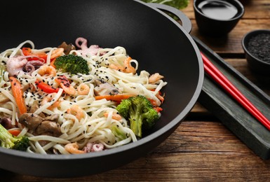 Stir fried noodles with seafood and vegetables in wok on wooden table, closeup
