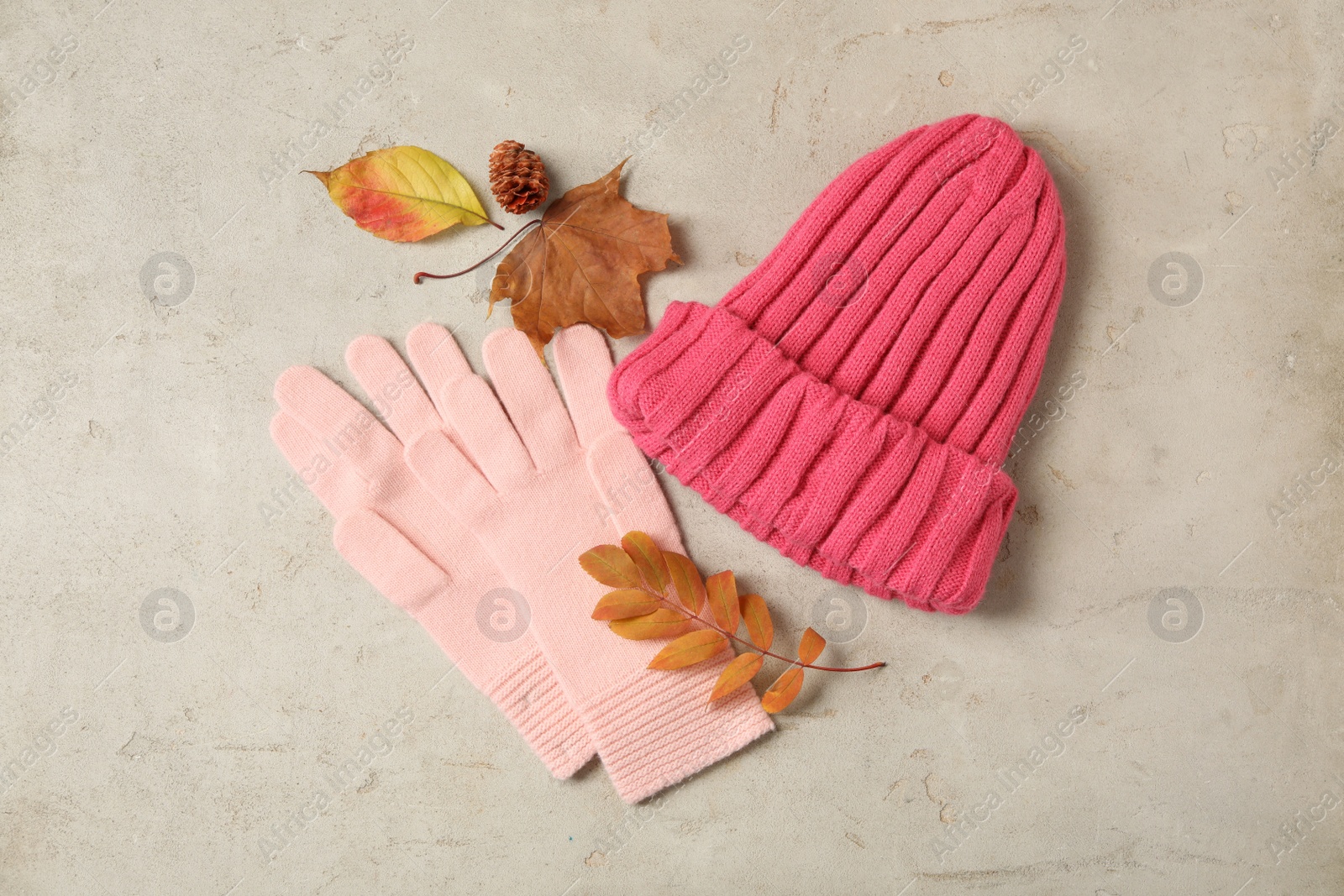 Photo of Stylish pink woolen gloves, hat and dry leaves on beige table, flat lay