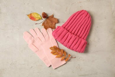 Stylish pink woolen gloves, hat and dry leaves on beige table, flat lay