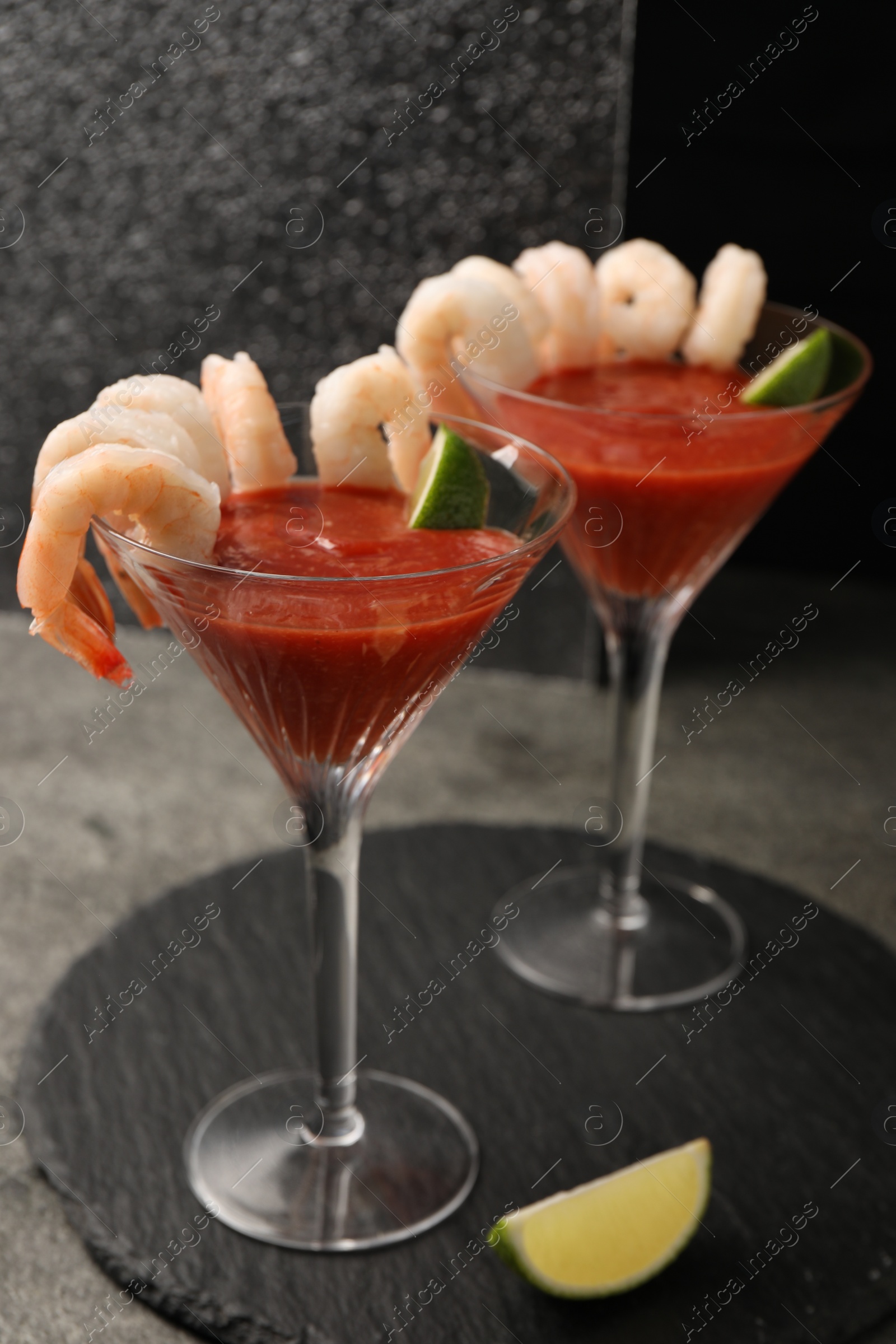 Photo of Tasty shrimp cocktail with sauce in glasses and lime on grey table